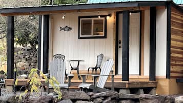 A log cabin with a porch, two Adirondack chairs, a small table, and a stone wall.