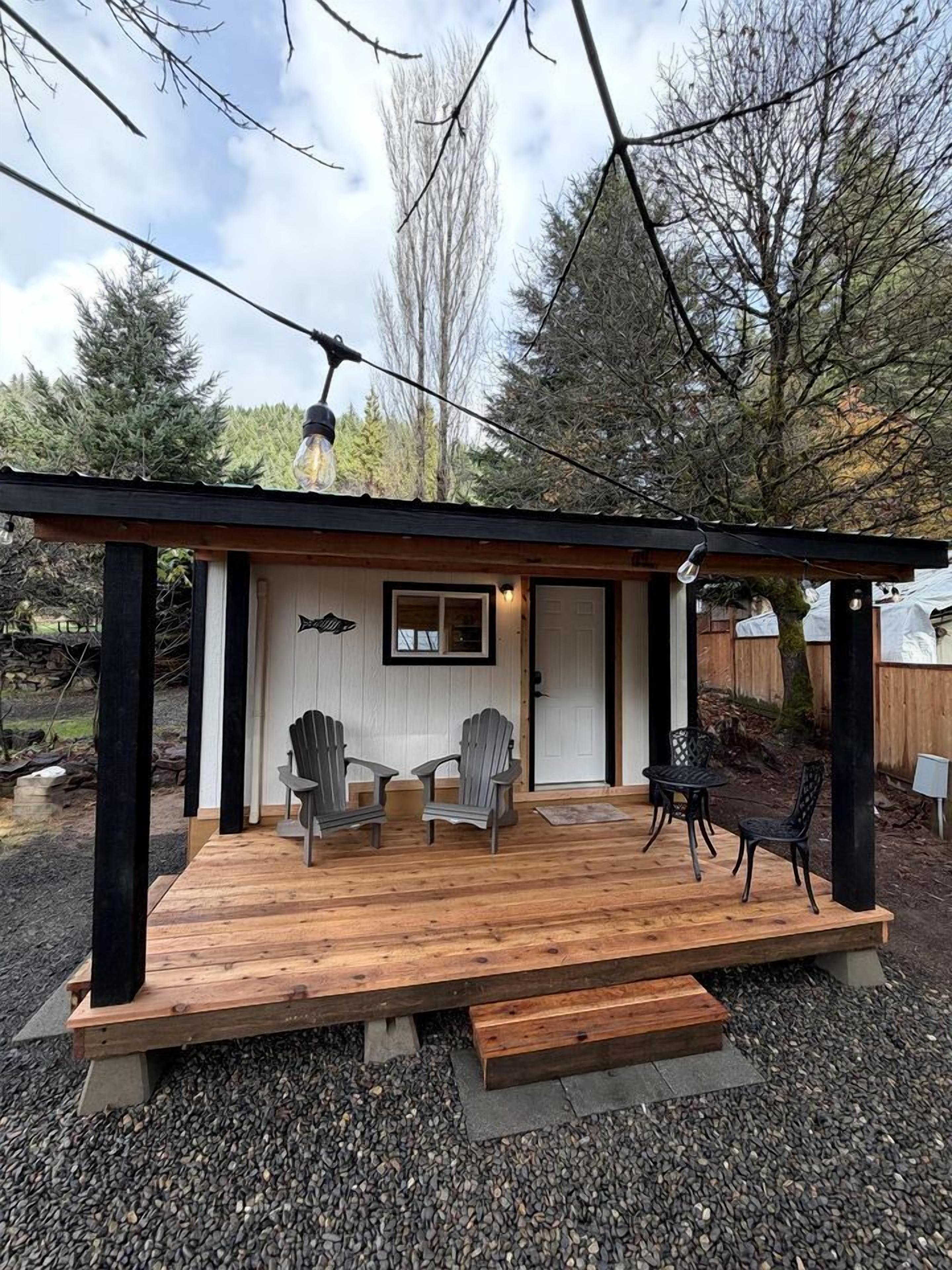A wooden deck with chairs and a table, a door with a fish sign, and a pergola with a light fixture.