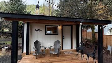 A wooden deck with chairs and a table, a door with a fish sign, and a pergola with a light fixture.
