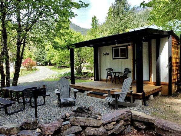 A rustic cabin with a deck, outdoor seating, and a view of a forested area.