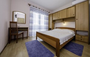 Ein Schlafzimmer mit Bett, Holzschrank, Schreibtisch, Stuhl und Spiegel.