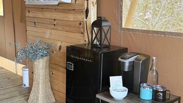 Ett litet rum med träpanel på väggarna, en svart kaffemaskin, ett litet bord med en skål och muggar, och ett fönster med utsikt över träd.