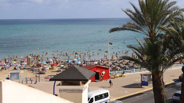 Une plage avec des parasols, une tour de surveillance pour les sauveteurs et un bâtiment rouge.