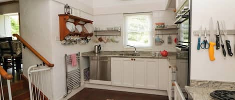 A kitchen with white cabinets, a stainless steel sink, a hanging pot rack, and a variety of kitchen utensils.