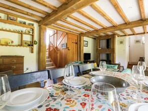 A dining area with wooden beams, a table set for four, and a staircase leading to another room. - Cynefin (Newport)