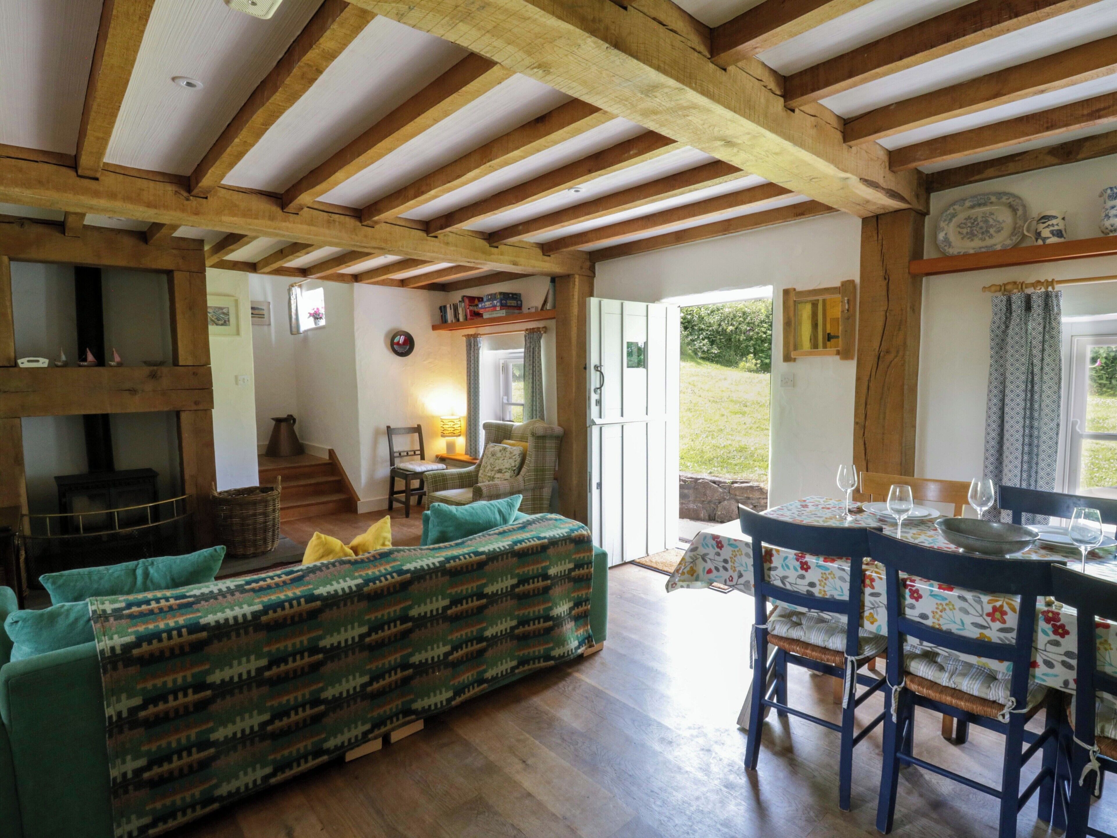 Un salon chaleureux avec un plafond en bois, un canapé, une table à manger avec des chaises et une vue sur l’extérieur, visible à travers une porte.