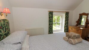 Ein Schlafzimmer mit Bett, Heizkörper, einem Fenster mit Vorhängen, einem Schminktisch und einer Lampe.