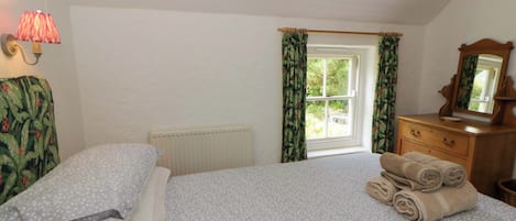 A bedroom with a bed, a radiator, a window with curtains, a dresser, and a lamp.
