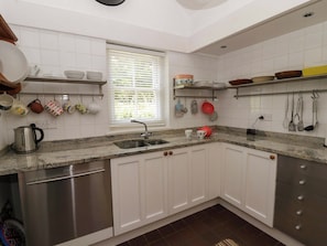 A kitchen with white cabinets, a granite countertop, a stainless steel sink, and a window with blinds. - Cynefin (Newport)