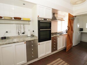A modern kitchen with white cabinets, a double oven, a gas stove, and a microwave. - Cynefin (Newport)
