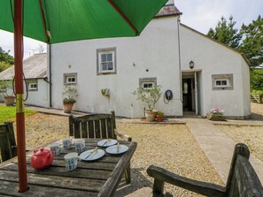 A white building with a door, windows, and a small garden area with a table set for tea. - Cynefin (Newport)