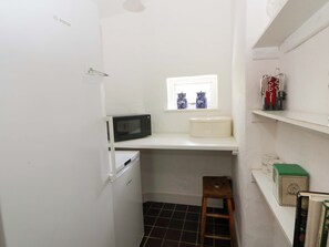 A compact kitchen with a microwave, a small window, and a white refrigerator. - Cynefin (Newport)