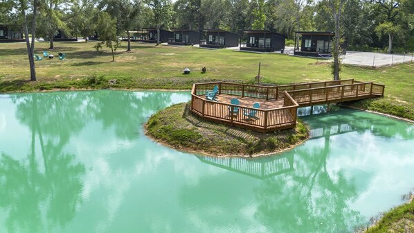Terraza a la orilla del lago con sillas y un puente de madera que conecta con una pequeña isla.