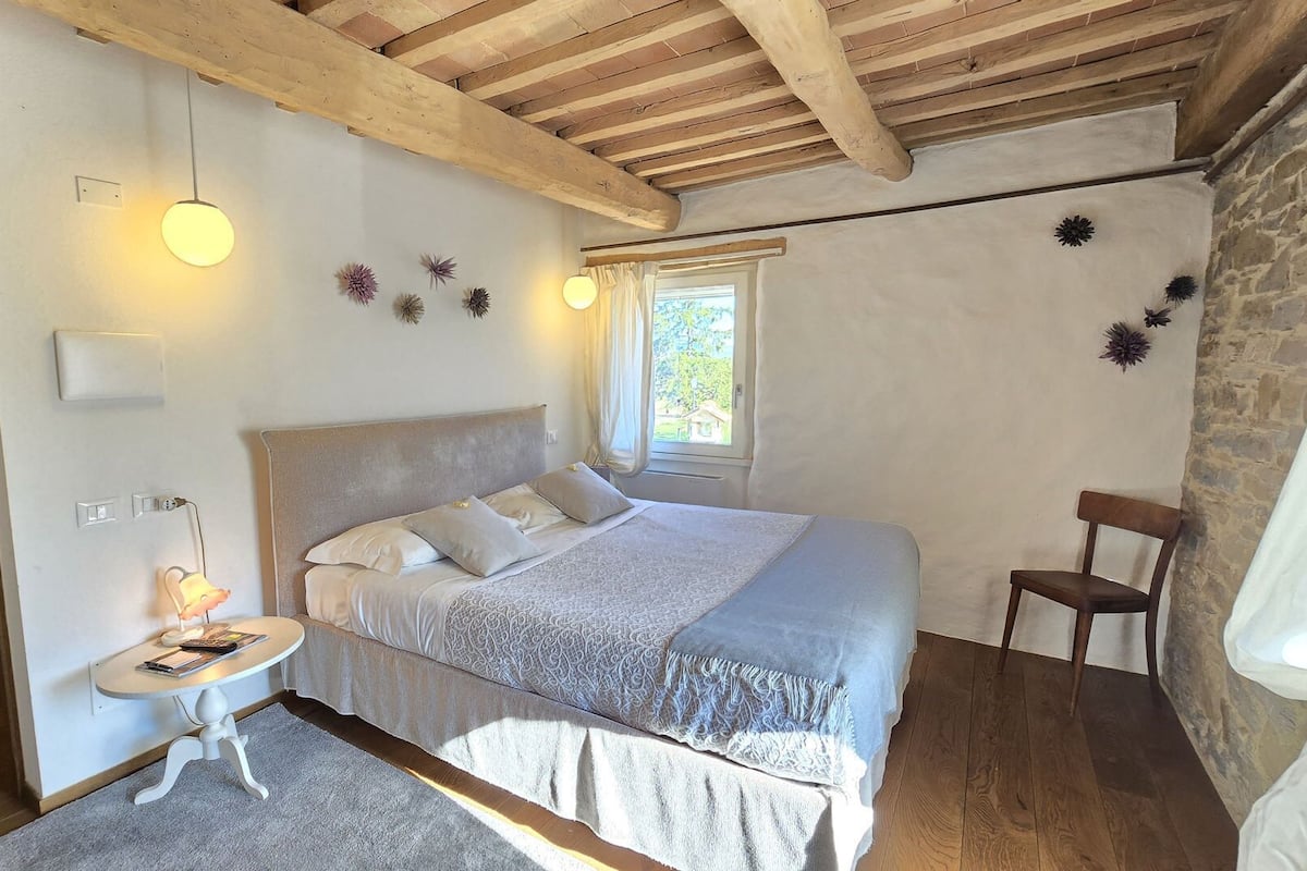 Una camera da letto con un letto, un comodino, una lampada e una finestra con tende.