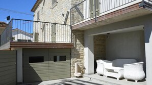A stone building with a balcony, a gated garage, and outdoor wicker furniture. - Cà Maina (Santa Sofia)
