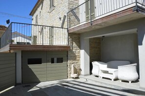 A stone building with a balcony, a gated garage, and outdoor wicker furniture. - Cà Maina (Santa Sofia)