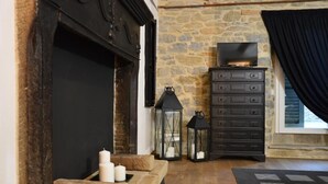 A stone fireplace with candles, a black TV, and a dark dresser in a room with wooden flooring. - Cà Maina (Santa Sofia)