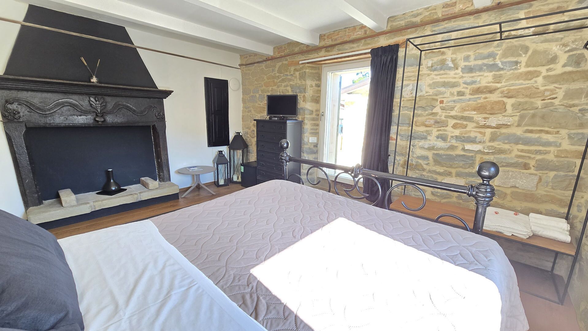 A bedroom with a stone wall, a fireplace, a bed, a dresser, and a television.