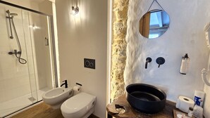 A bathroom with a shower, bidet, toilet, and a stone wall with a mirror. - Cà Maina (Santa Sofia)