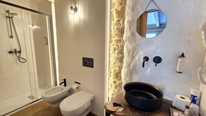 Un baño con ducha, bidé, inodoro y pared de piedra con espejo.