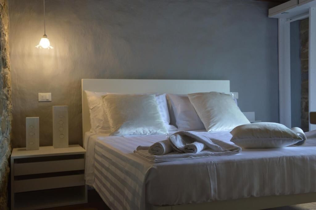 Un lit bien fait, avec des oreillers et des serviettes pliées, une table de chevet avec une lampe et un luminaire fixé au mur.