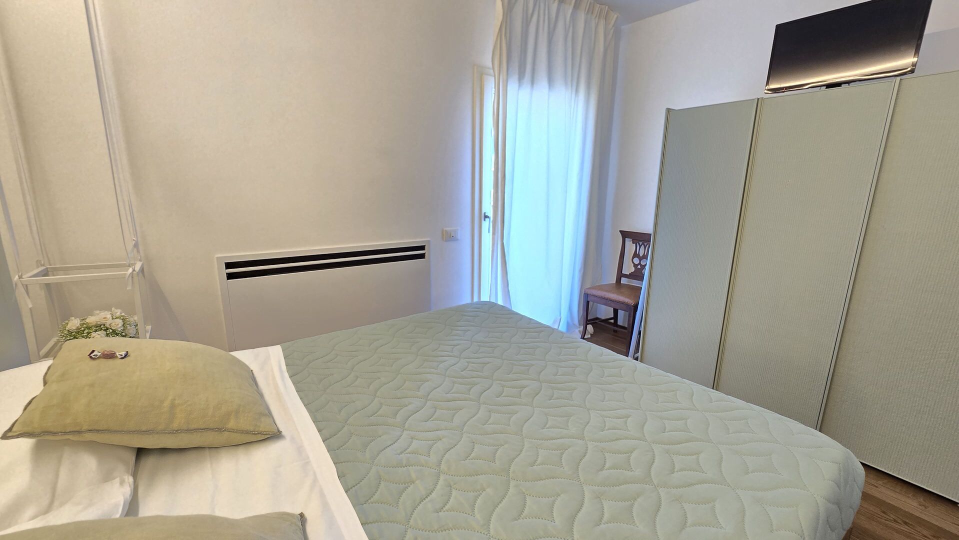 A bedroom with a bed, a chair, a wardrobe, and a radiator.