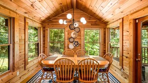 Eine Holzhütte mit Esstisch und Stühlen, großen Fenstern und einer Deckenleuchte.