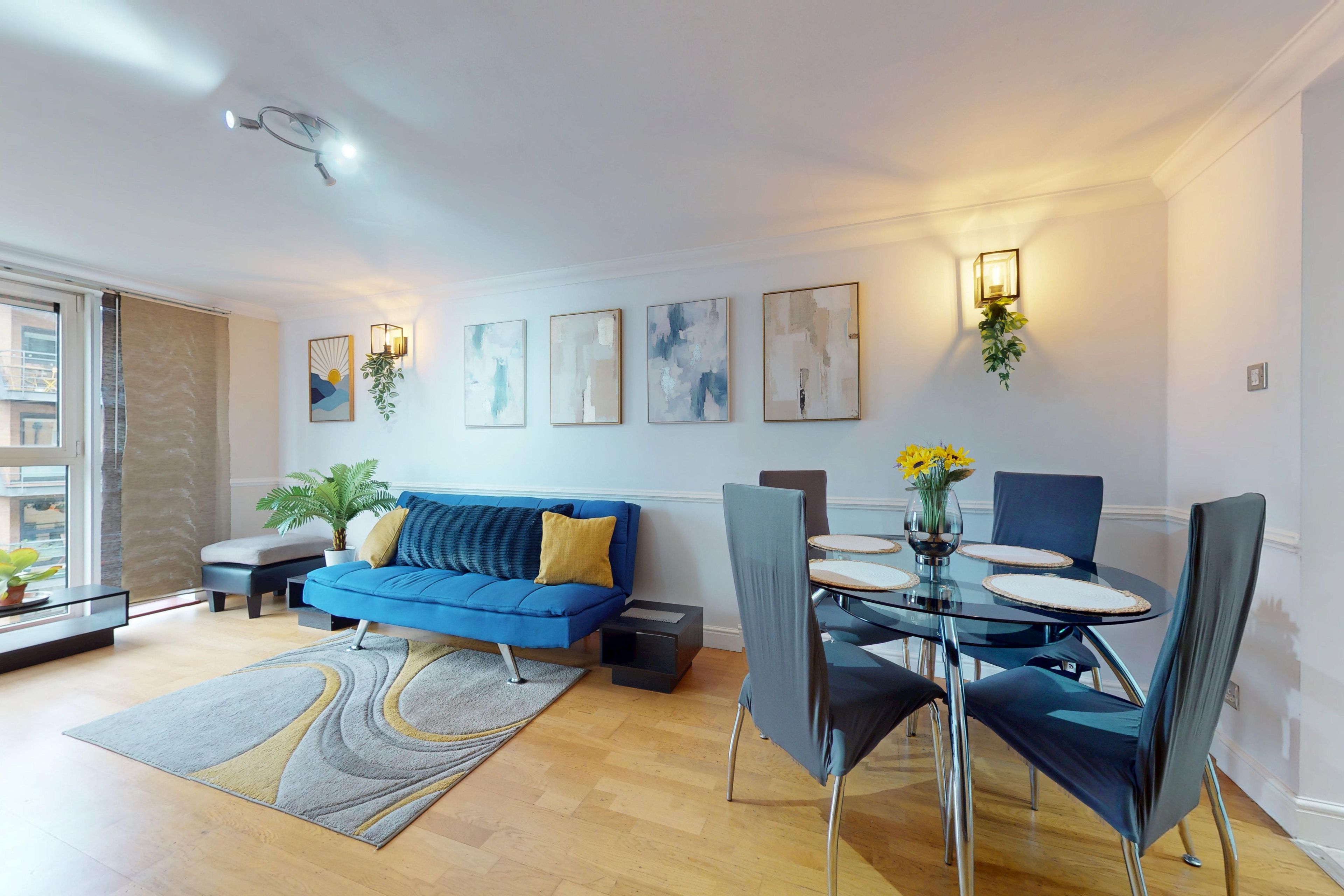A modern living room with a blue sofa, a dining table with chairs, and artwork on the walls.