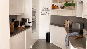 A modern kitchen with white cabinets, a coffee machine, a toaster, and a trash bin. - 2BR w/ Private Balcony & River Thames Views (London)