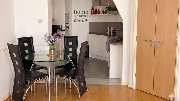 A dining area with a glass table and black chairs, a kitchen with white cabinets, and a wooden door. - 2BR w/ Private Balcony & River Thames Views (London)