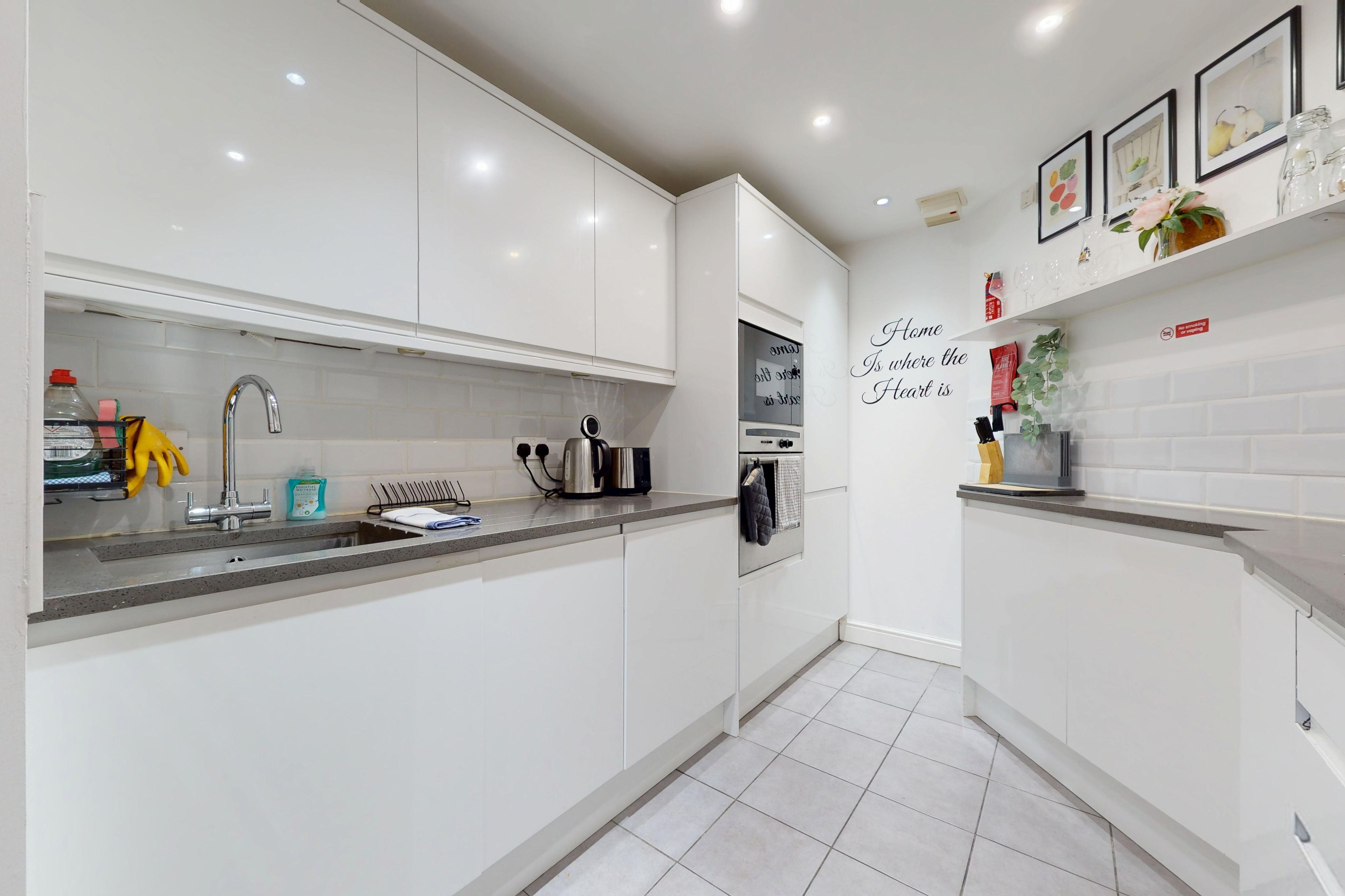 A modern kitchen with white cabinets, a stainless steel sink, and a built-in oven.