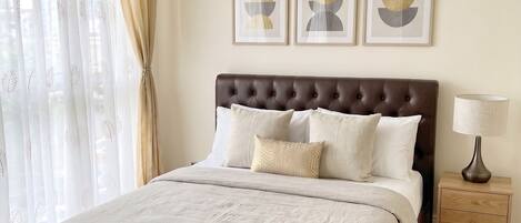A bedroom with a bed, a nightstand, a lamp, and three framed artworks on the wall.