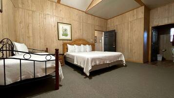 A bedroom with two beds, wooden walls, a framed picture, and a door leading to another room.