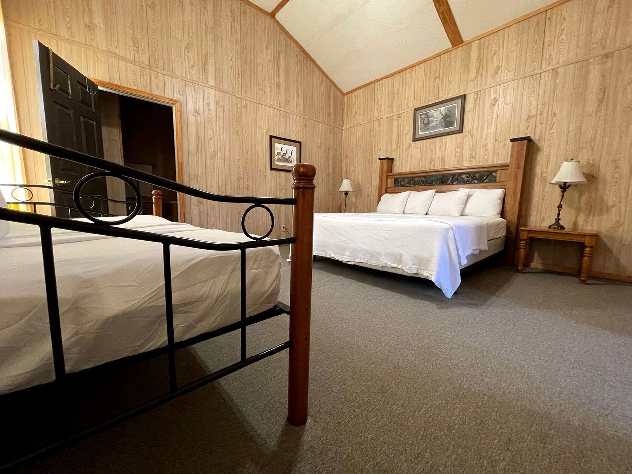 A room with two beds, wooden paneling, a door, and a framed picture on the wall.