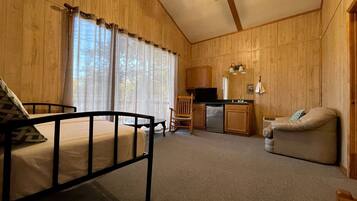 A room with a bed, a chair, a sofa, a kitchenette, and a ceiling fan.