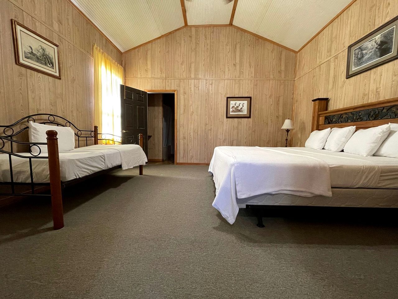 Una habitación con dos camas individuales, techo de madera y una puerta que da a otra habitación.