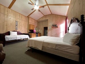 A room with a large bed, a smaller bed, a desk, and a ceiling fan.