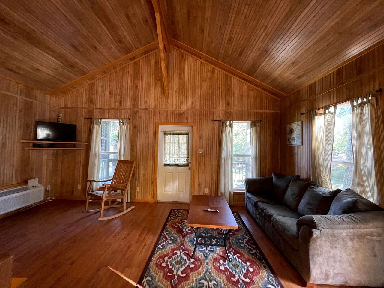A wooden-paneled room with a sofa, a rocking chair, a table, and a television.