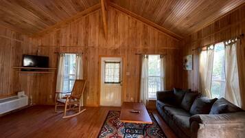 A wooden-paneled room with a sofa, a rocking chair, a table, and a television.