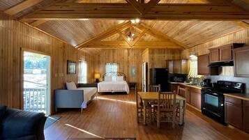 A cabin interior with a wooden interior, a bed, a dining table with chairs, a kitchen area, and a balcony.