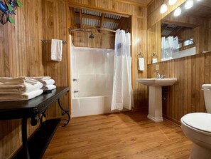 Une salle de bain aux murs lambrissés, équipée d’une baignoire, d’un lavabo, de toilettes et d’un miroir.