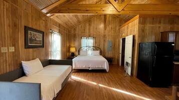 A wooden-paneled room with two beds, a refrigerator, and a small kitchen area.