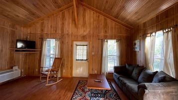 A wooden-paneled room with a sofa, a rocking chair, a table, and a television.