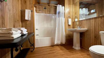 A wooden-paneled bathroom with a bathtub, a sink, a toilet, and a mirror.