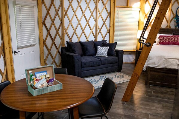 A cozy room with a dark blue sofa, a wooden table with a basket, and a bed with a white sheet.