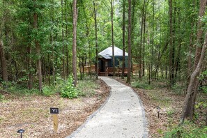 A forested area with a paved path leading to a cabin-like structure.