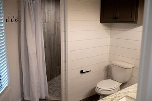 A bathroom with a white toilet, a wooden shower enclosure, and a cabinet above the toilet.