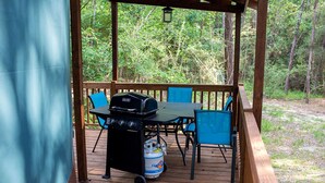 A wooden deck with a grill and chairs, surrounded by trees.