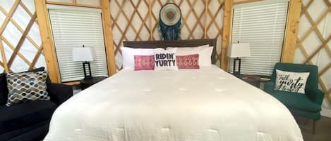 A bed with a white duvet, two pillows with text, a headboard, a wall with a lattice pattern, a window with blinds, a lamp, a chair with a cushion, and a decorative item on the wall.
