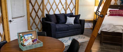 Una habitación acogedora con un sofá azul oscuro, una mesa de madera con una cesta y una cama con sábanas blancas.